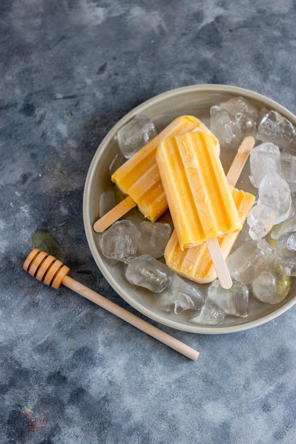 mango yogurt popsicles and ice on a grey plate.