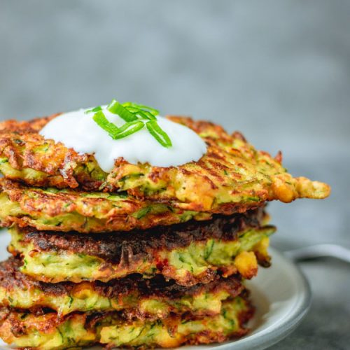 stack of crispy courgette and sweetcorn fritters on a plate.