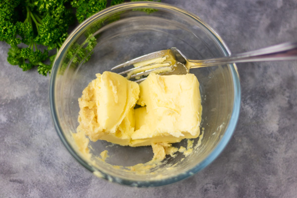 1 stick of butter and mashed roasted garlic in a bowl with fork.