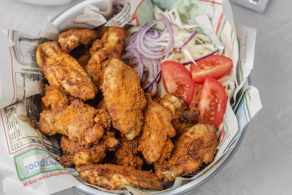 chicken wings suya served on old newspaper in a bowl with some salad on the side.