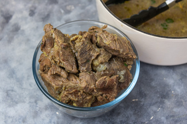 cooked meat in a glass bowl placed beside a pot.