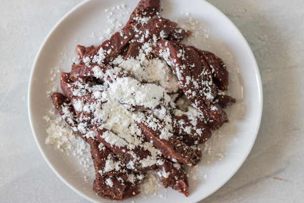 a plate of raw beef strips covered with corn flour.