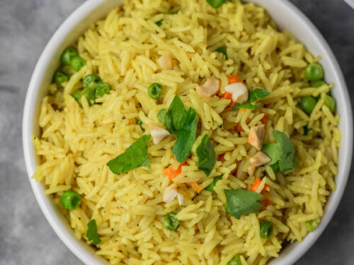 a bowl of yellow rice garnished with parsley and cashew nuts.