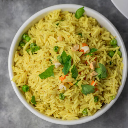 a bowl of yellow rice garnished with parsley and cashew nuts.