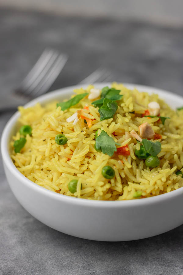 a bowl of yellow rice garnished with parsley and nuts.