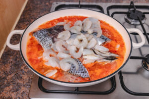 fresh shrimps and fish in red sauce placed over the stove top.