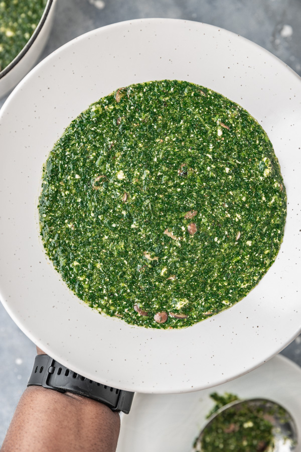 a hand holding up a plate of ewedu soup.